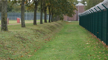 Blick entlang eines Innenzaun Richtung Sporthalle