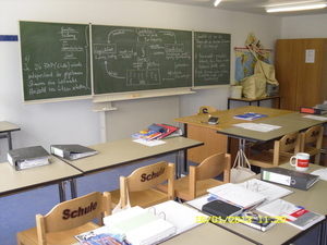 Klassenraum mit Tafel und Tischen mit Unterrichtsmaterialien
